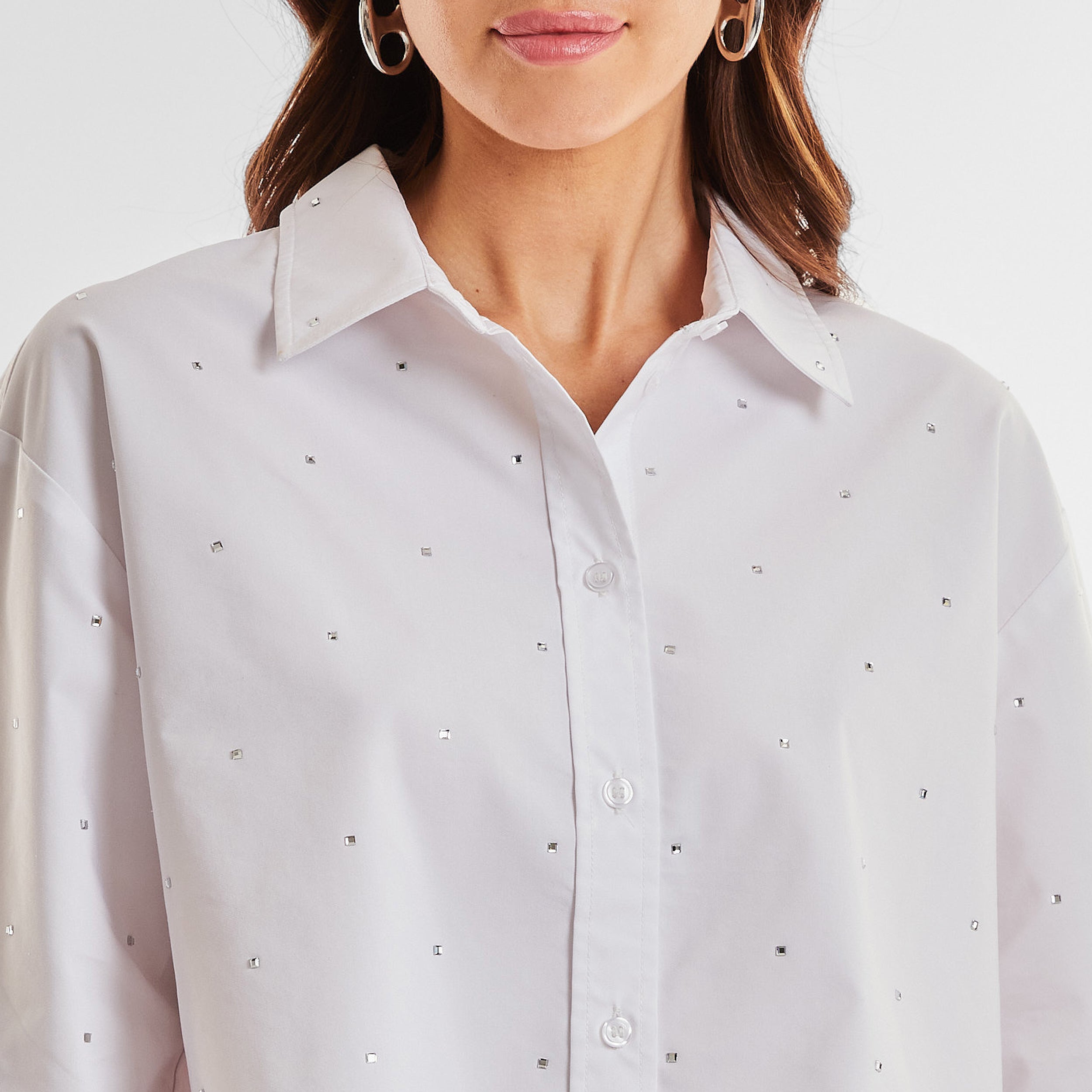 Close up front view of woman wearing a white cropped button down shirt with crystal embellishments.