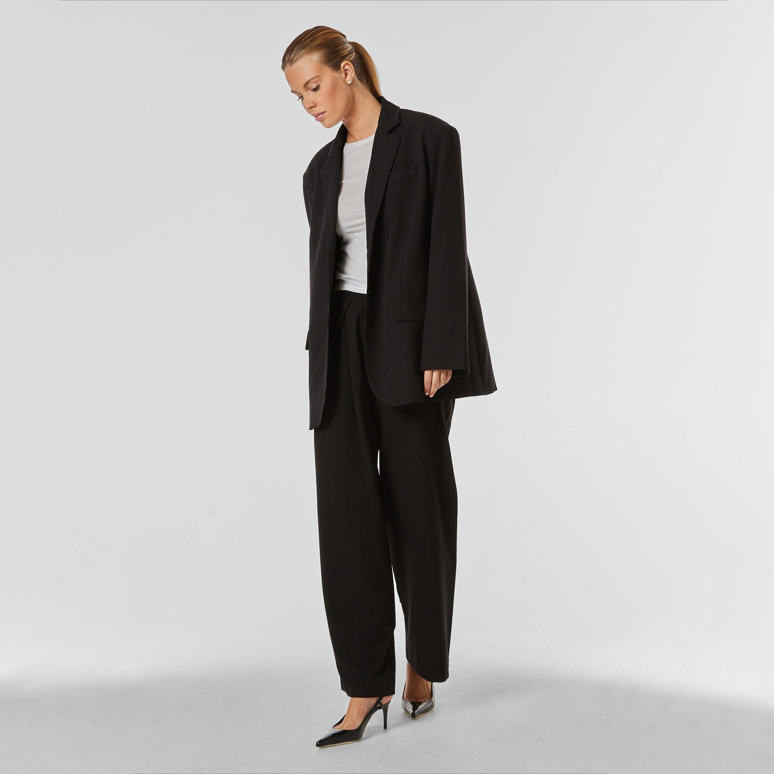 Full body view of woman wearing oversized black blazer and black trouser.