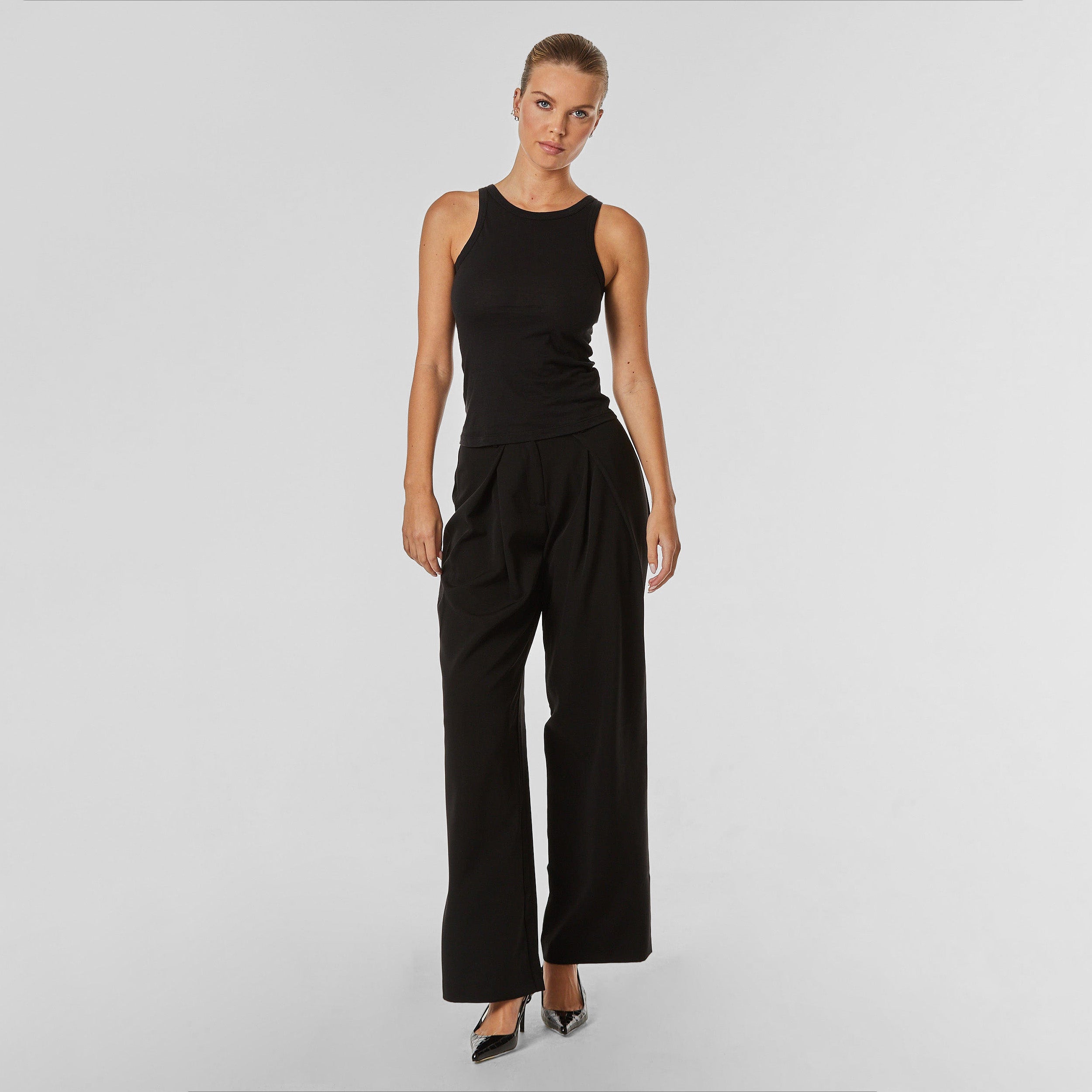 Full body front view of woman wearing pleated black trousers with stretch fabric
