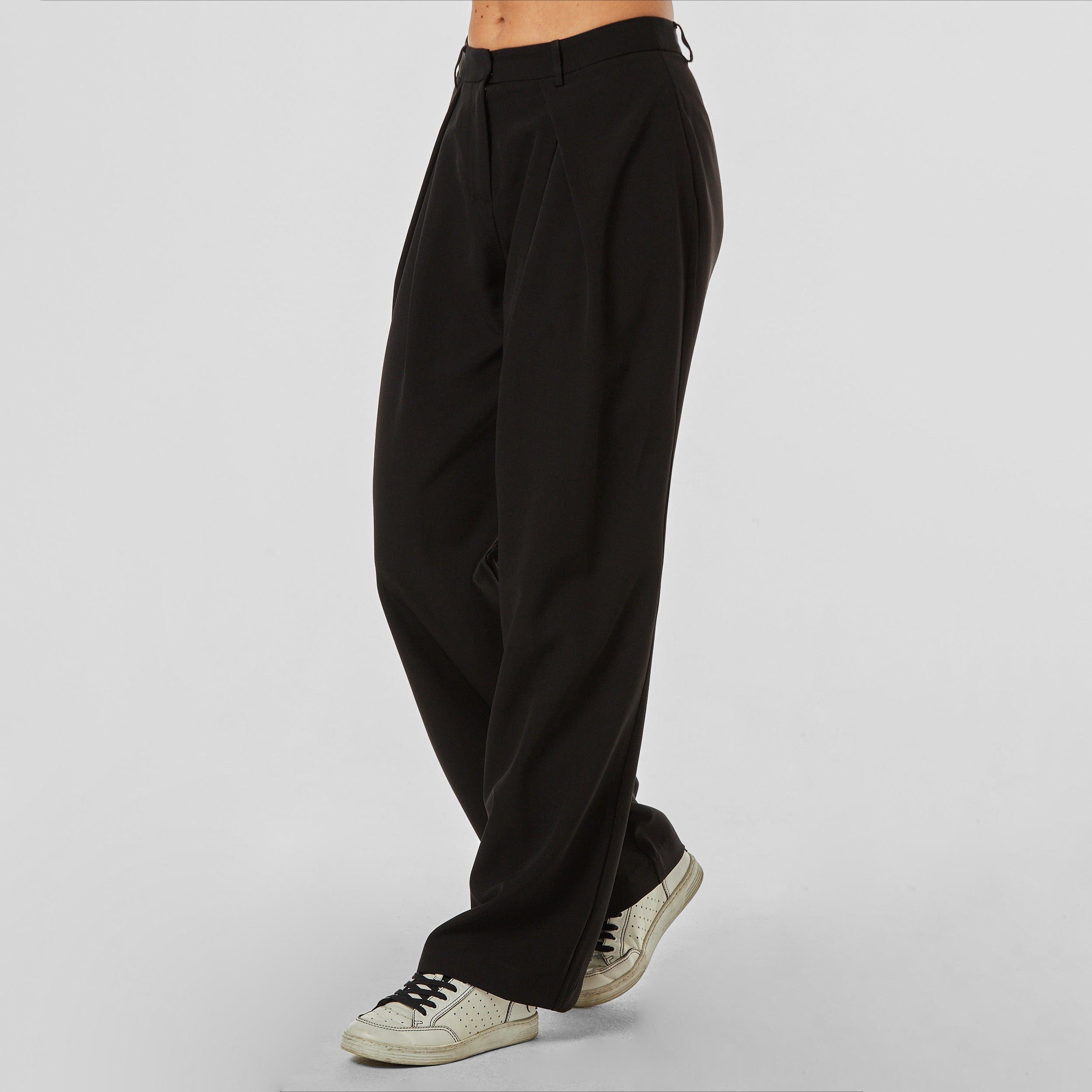 Side view of woman wearing pleated black trousers with stretch fabric