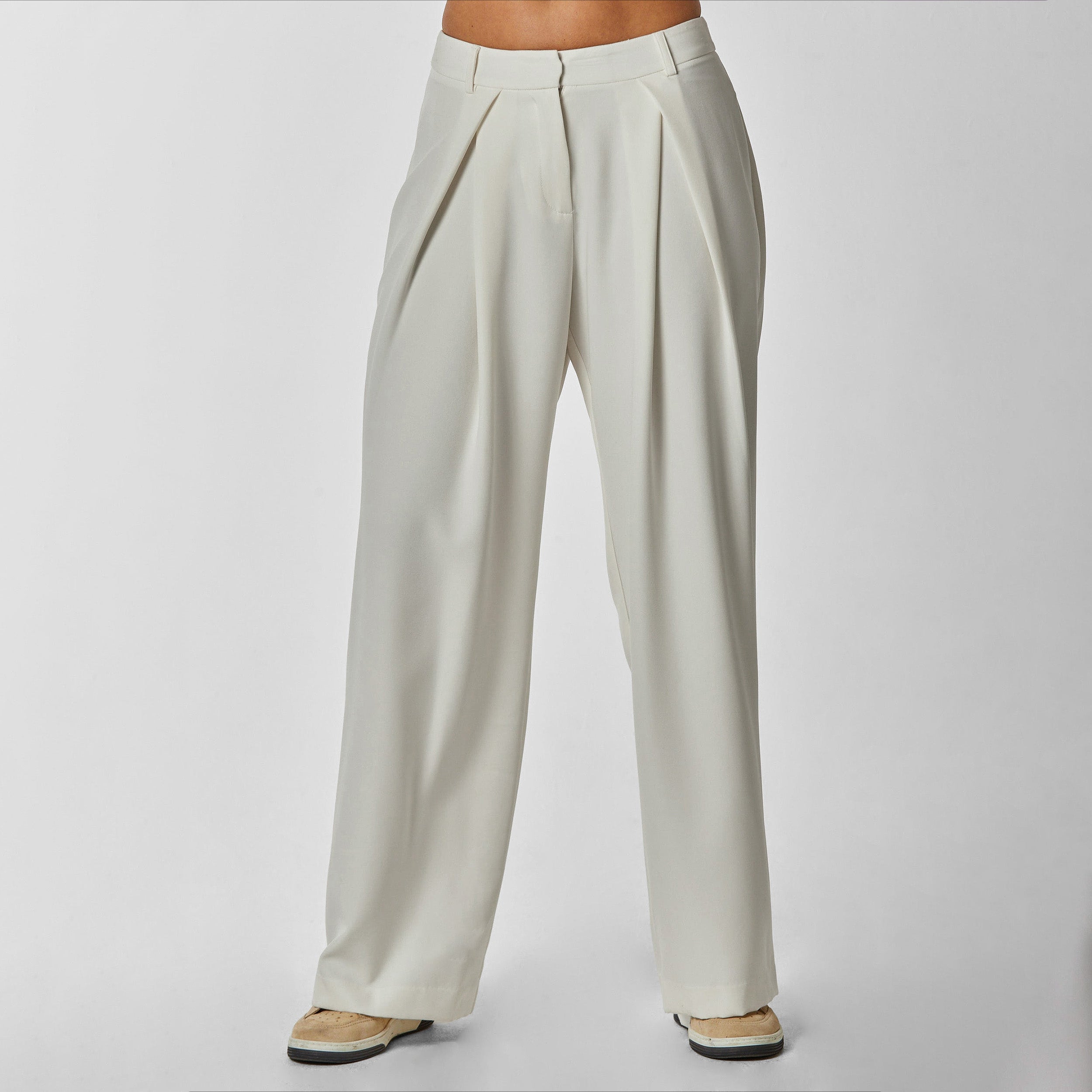 Front view of woman wearing pleated cream colored trousers with stretch fabric