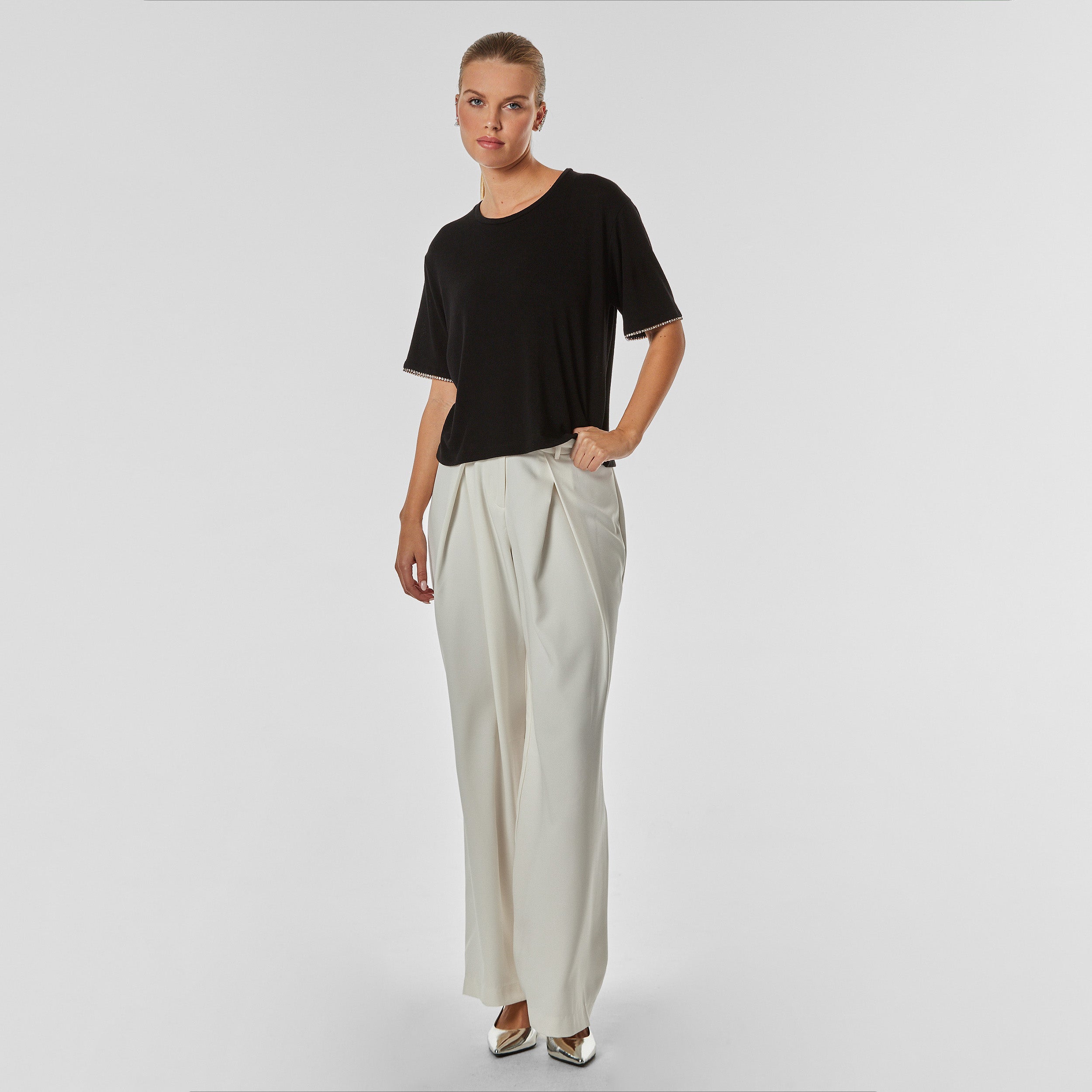 Full body view of woman wearing pleated cream colored trousers with stretch fabric