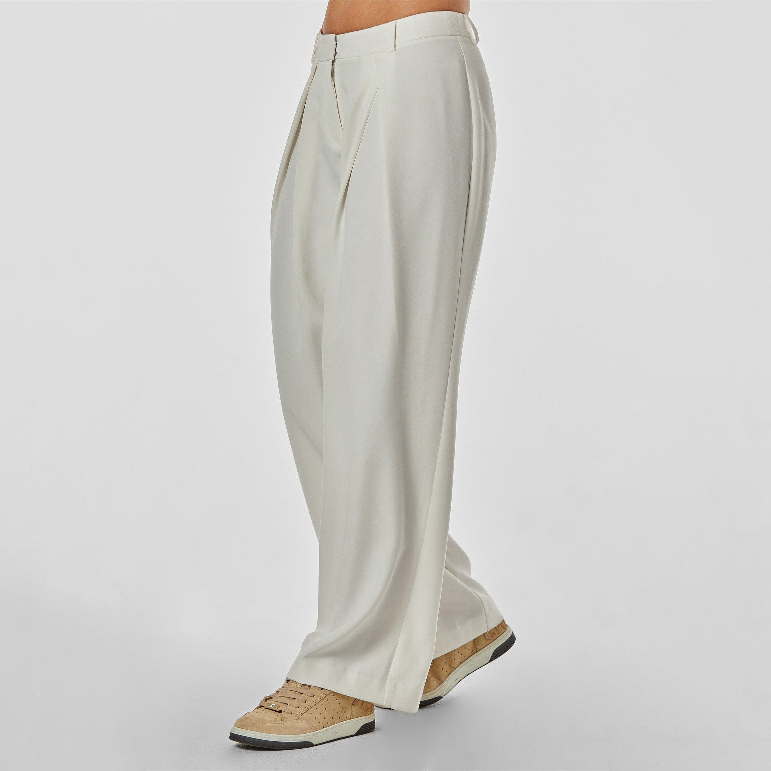 Side view of woman wearing pleated cream colored trousers with stretch fabric