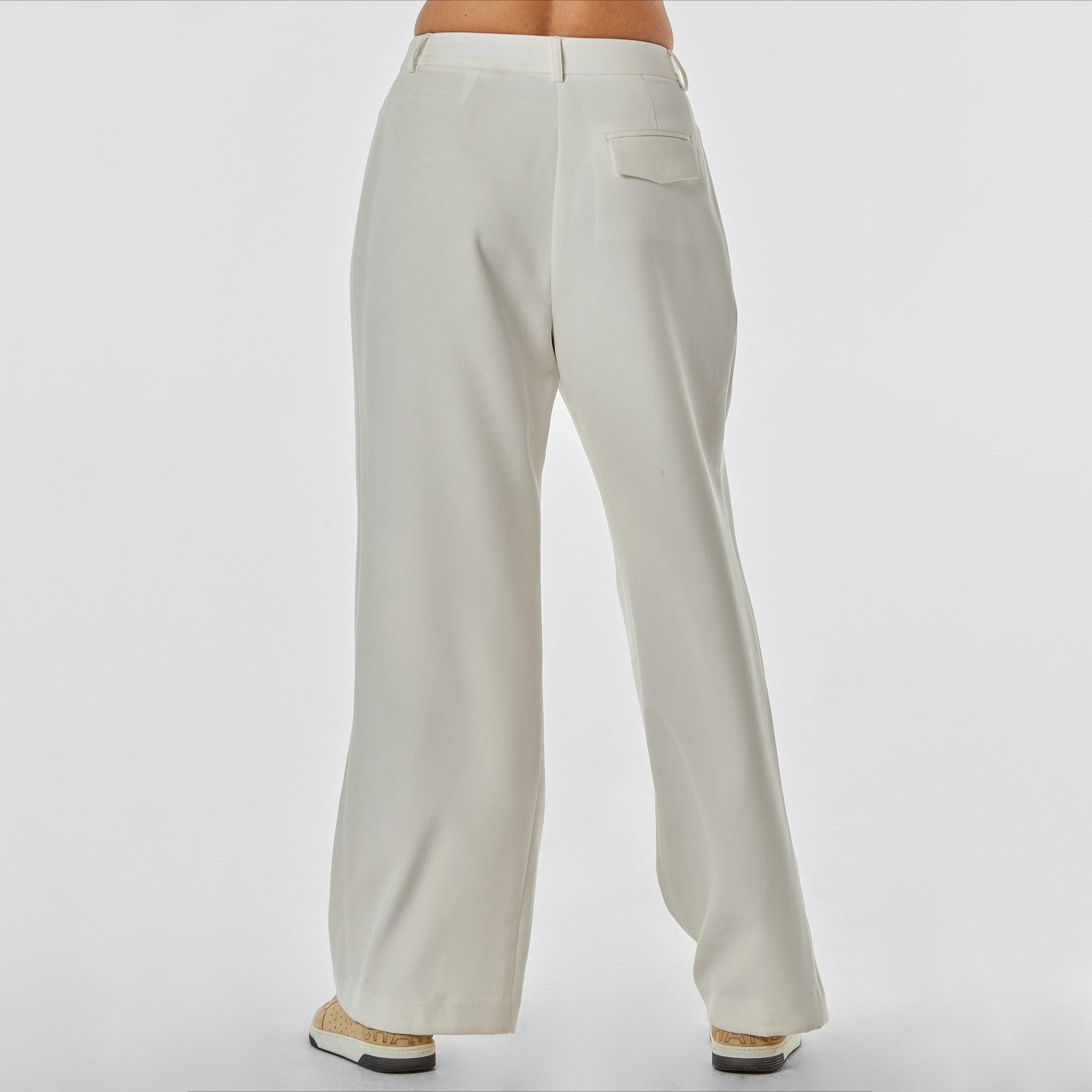 Rear view of woman wearing pleated cream colored trousers with stretch fabric