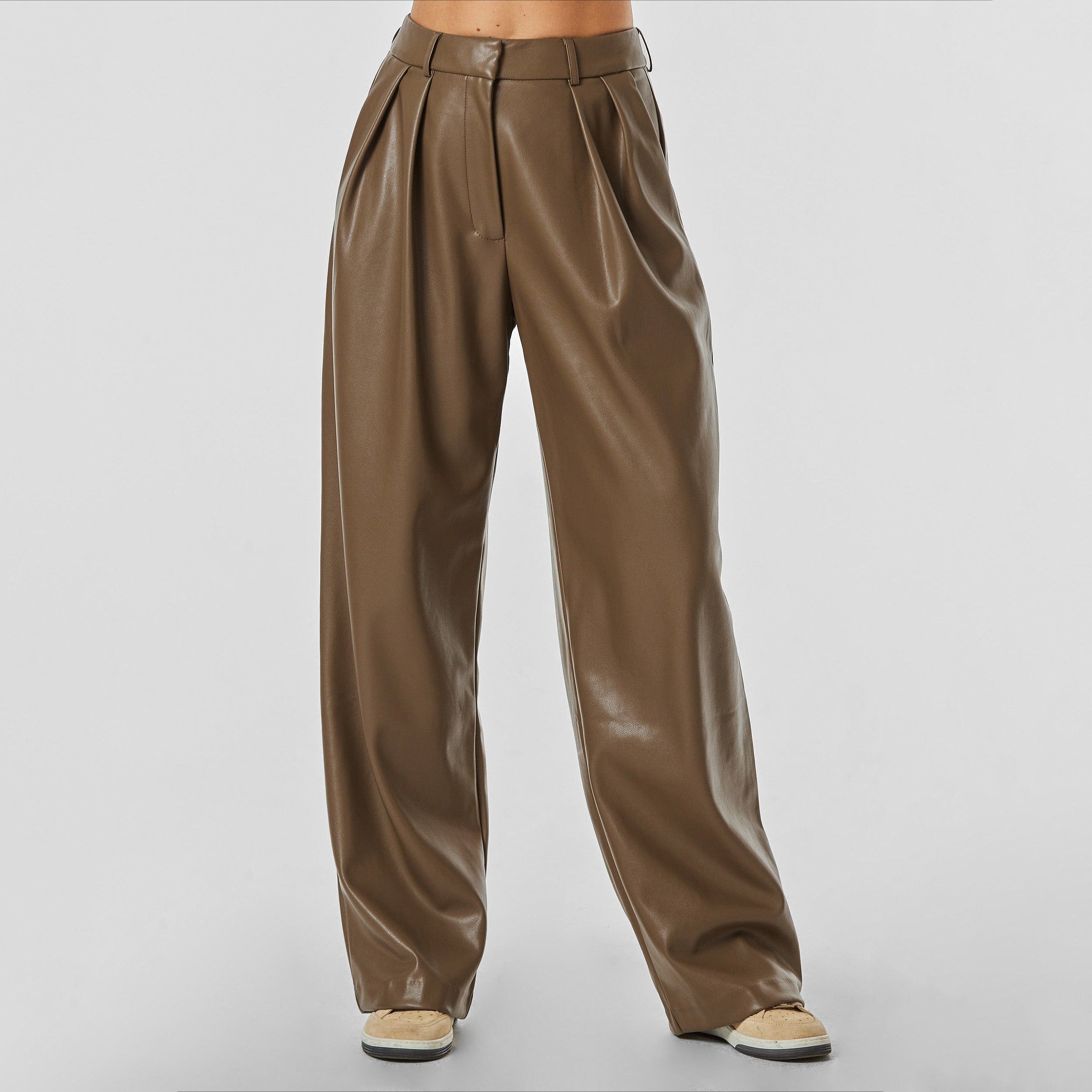 Front view of woman wearing brown high rise vegan leather pleated trousers.