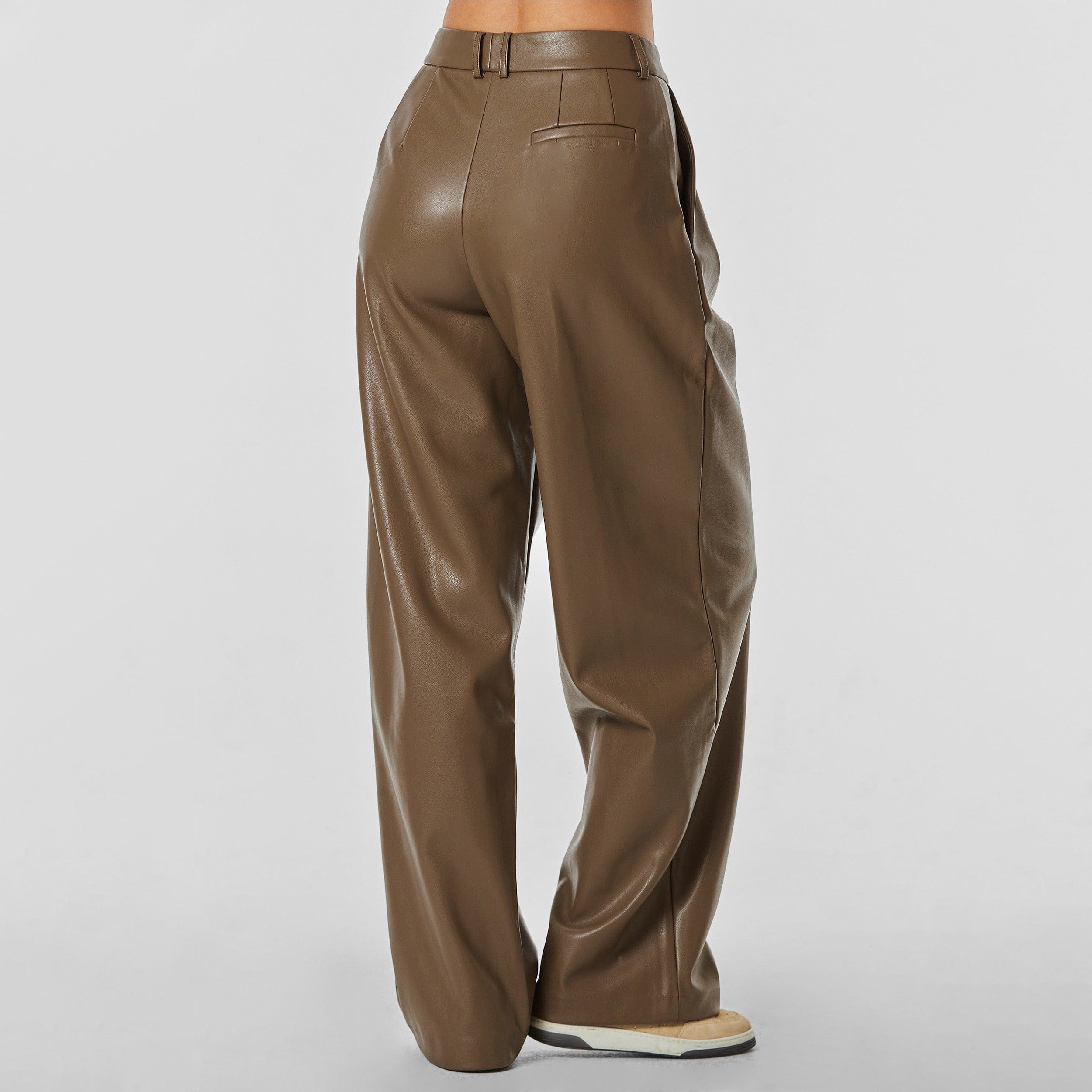 Rear view of woman wearing brown high rise vegan leather pleated trousers.