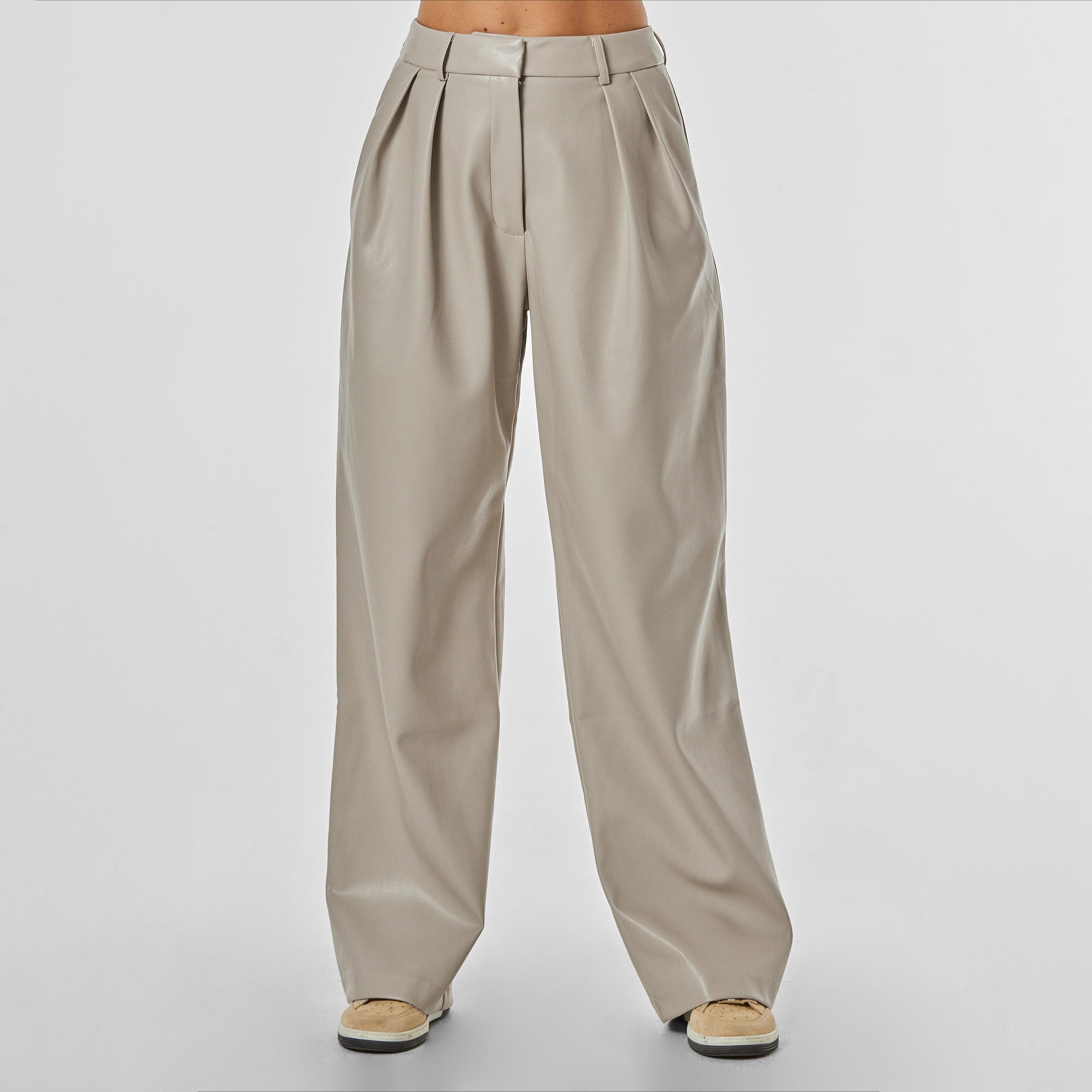 Front view of woman wearing beige colored high rise vegan leather pleated trousers.