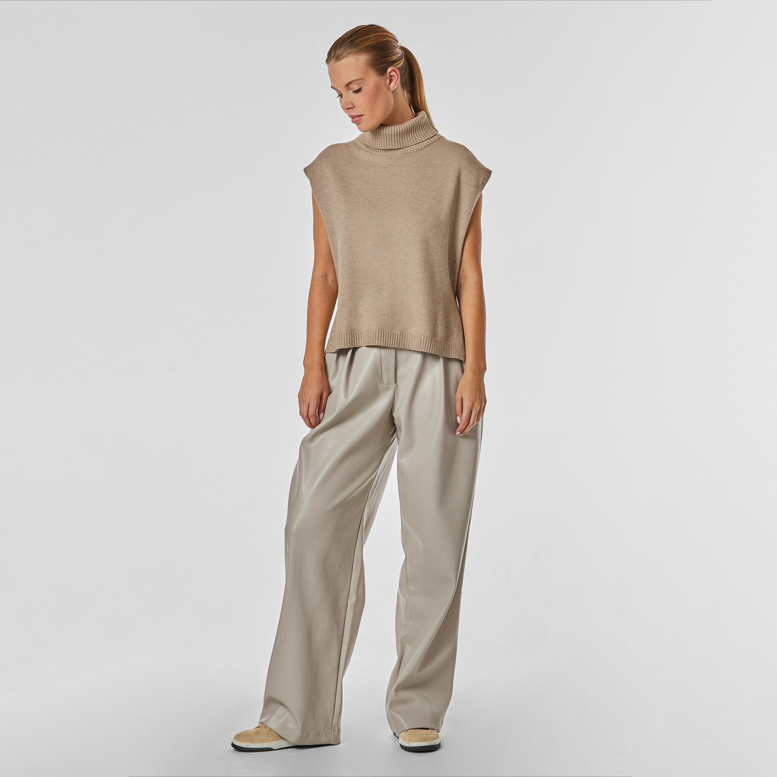 Full body front view of woman wearing pleated high rise faux leather cream trouser.
