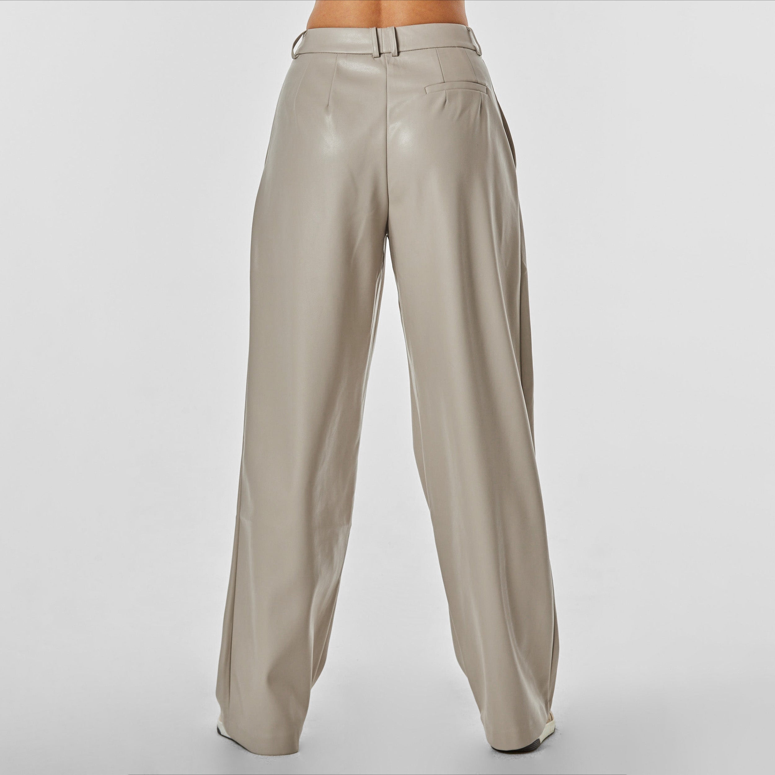 Rear view of woman wearing beige colored high rise vegan leather pleated trousers.