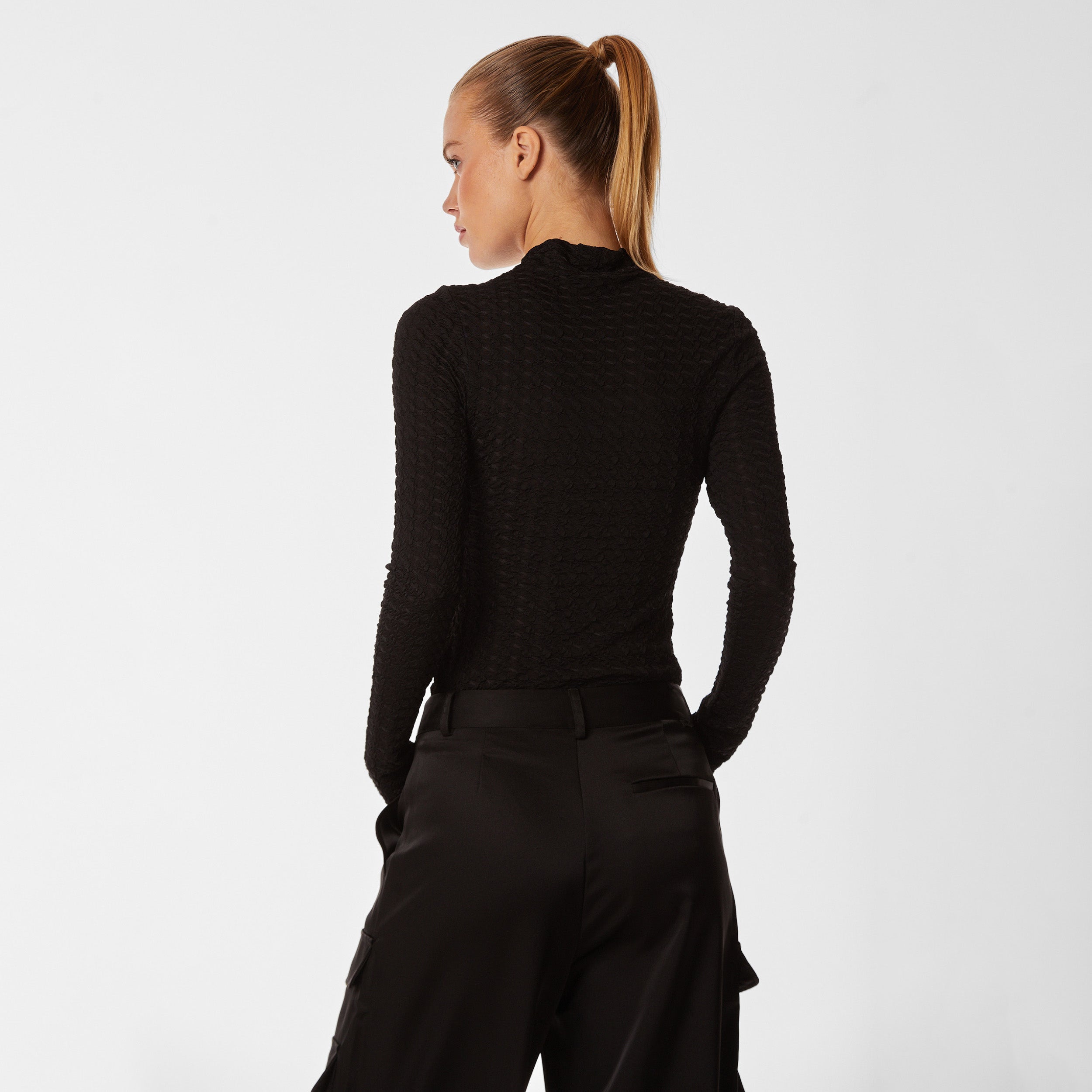 Rear view of woman wearing black stretch mesh textured turtleneck sweater