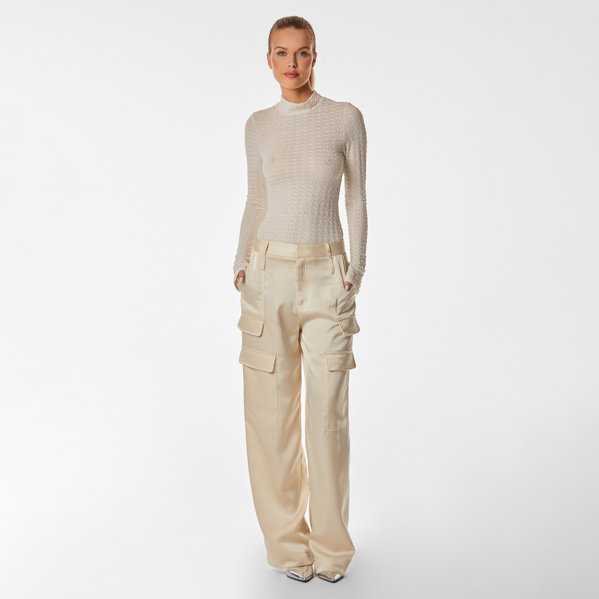 Woman wearing ivory stretch mesh textured turtleneck sweater and pearl satin cargo pant