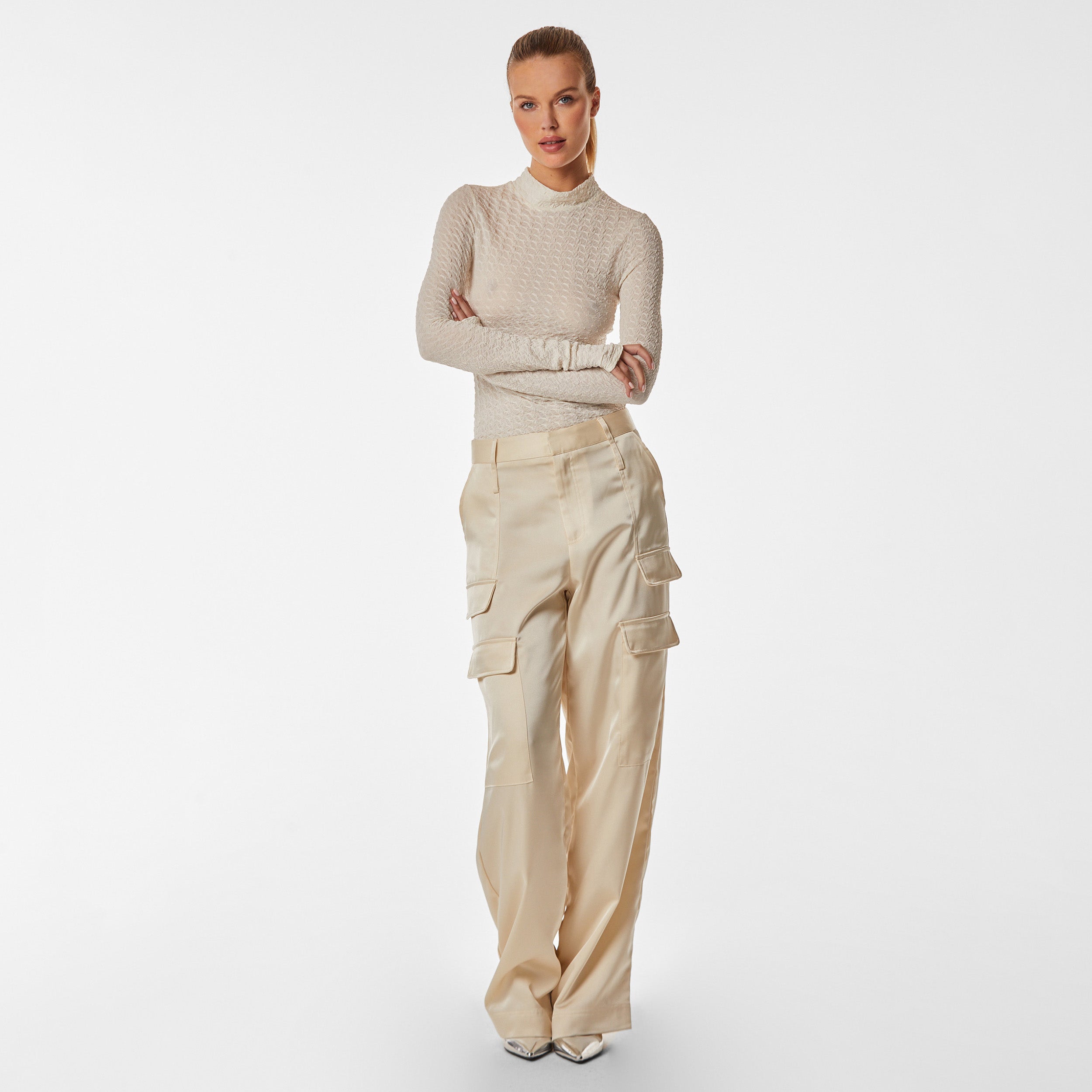 Full body view of woman wearing ivory stretch mesh textured turtleneck sweater and pearl satin cargo pant