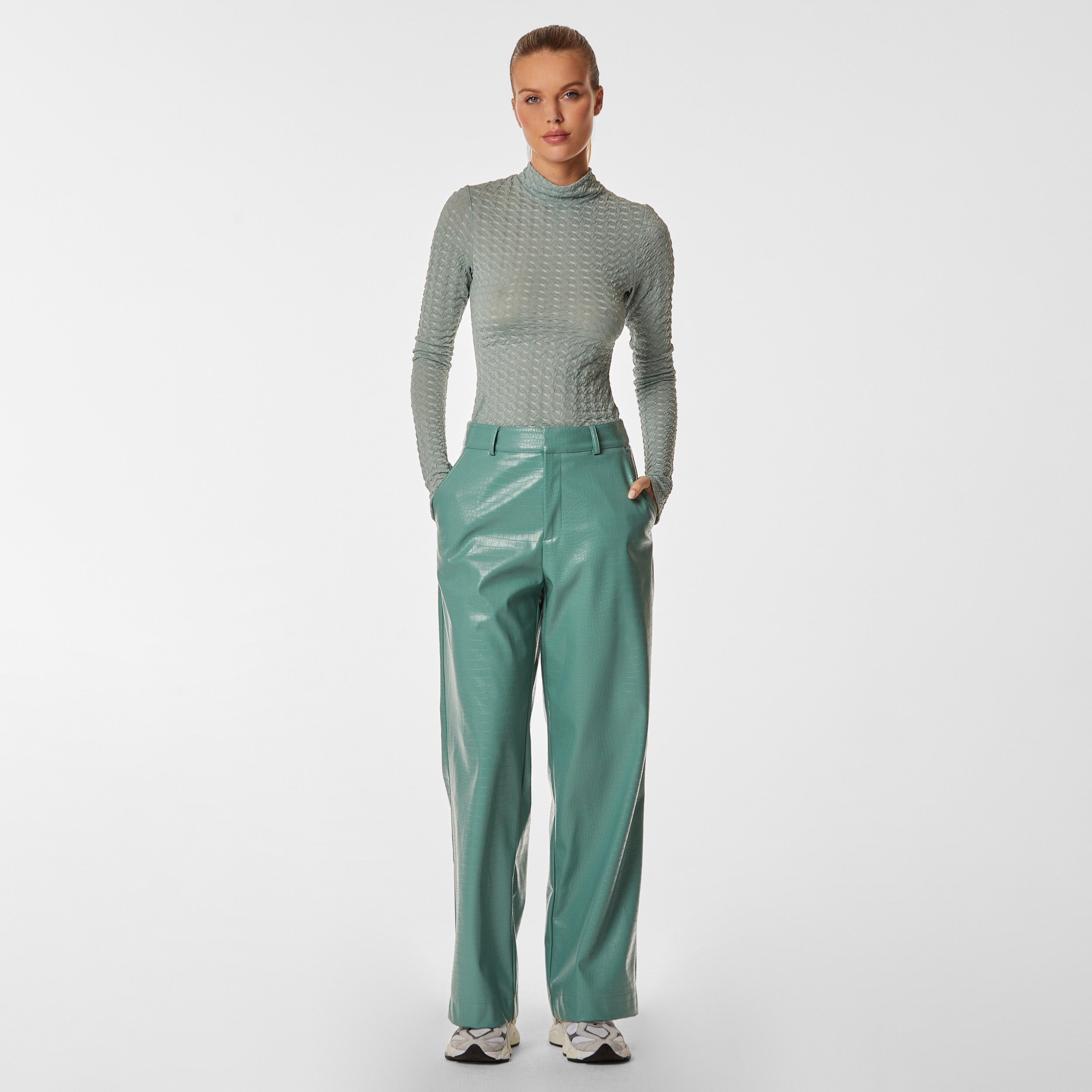 Fully body view of woman wearing green stretch mesh textured turtleneck sweater and mint green croco embossed faux leather pant.