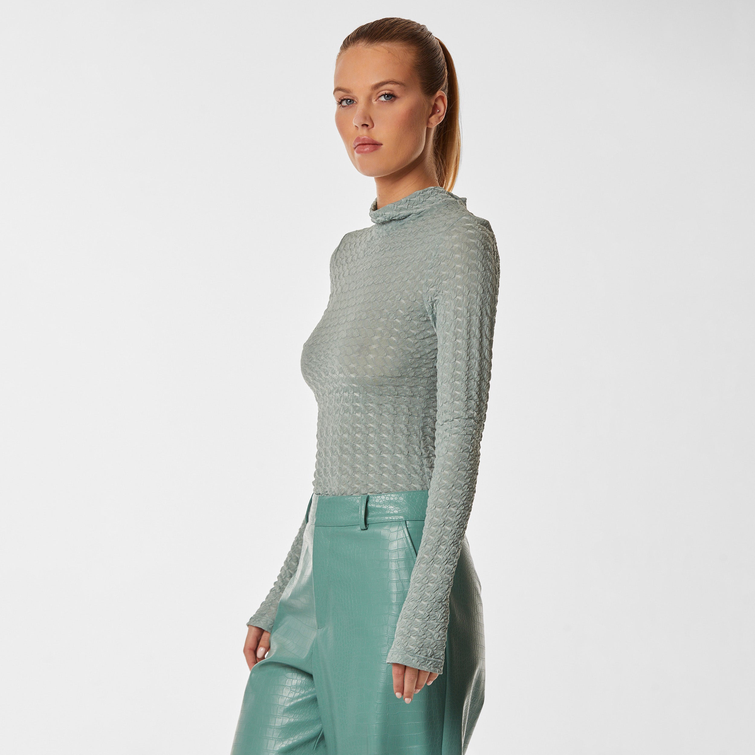 3/4 side view of woman wearing green stretch mesh textured turtleneck sweater