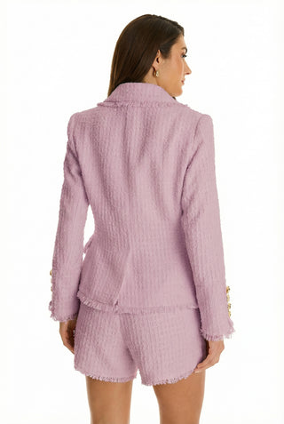 A woman with long brown hair is seen from the back wearing the Giselle Single Breasted Tweed Blazer in blush, featuring a textured finish and padded shoulders, paired with matching shorts against a plain white background.