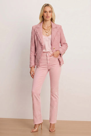 A woman with blonde hair and a neutral expression stands against a plain background wearing the Giselle Single Breasted Tweed Blazer in blush, styled with a light pink satin top, pink jeans, layered gold necklaces, and nude heels.