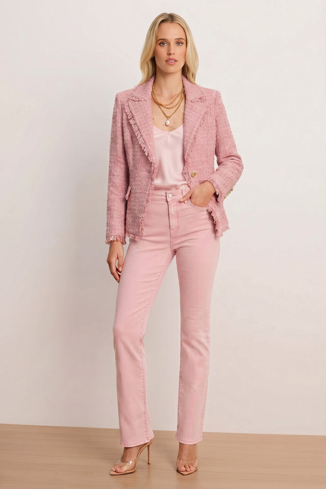 A woman with blonde hair and a neutral expression stands against a plain background wearing the Giselle Single Breasted Tweed Blazer in blush, styled with a light pink satin top, pink jeans, layered gold necklaces, and nude heels.