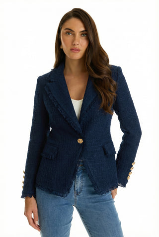 A woman with long brown hair wears the Giselle Single Breasted Tweed Blazer in navy, featuring gold buttons, paired with a white top and blue jeans. She stands against a white background.