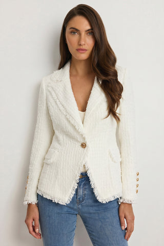 A woman with long brown hair wears the Giselle Single Breasted Tweed Blazer - White over a white top and blue jeans, embodying modern power dressing as she stands against a plain light background.