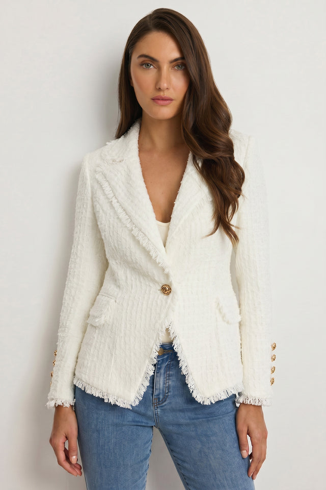 A woman with long brown hair wears the Giselle Single Breasted Tweed Blazer - White over a white top and blue jeans, embodying modern power dressing as she stands against a plain light background.