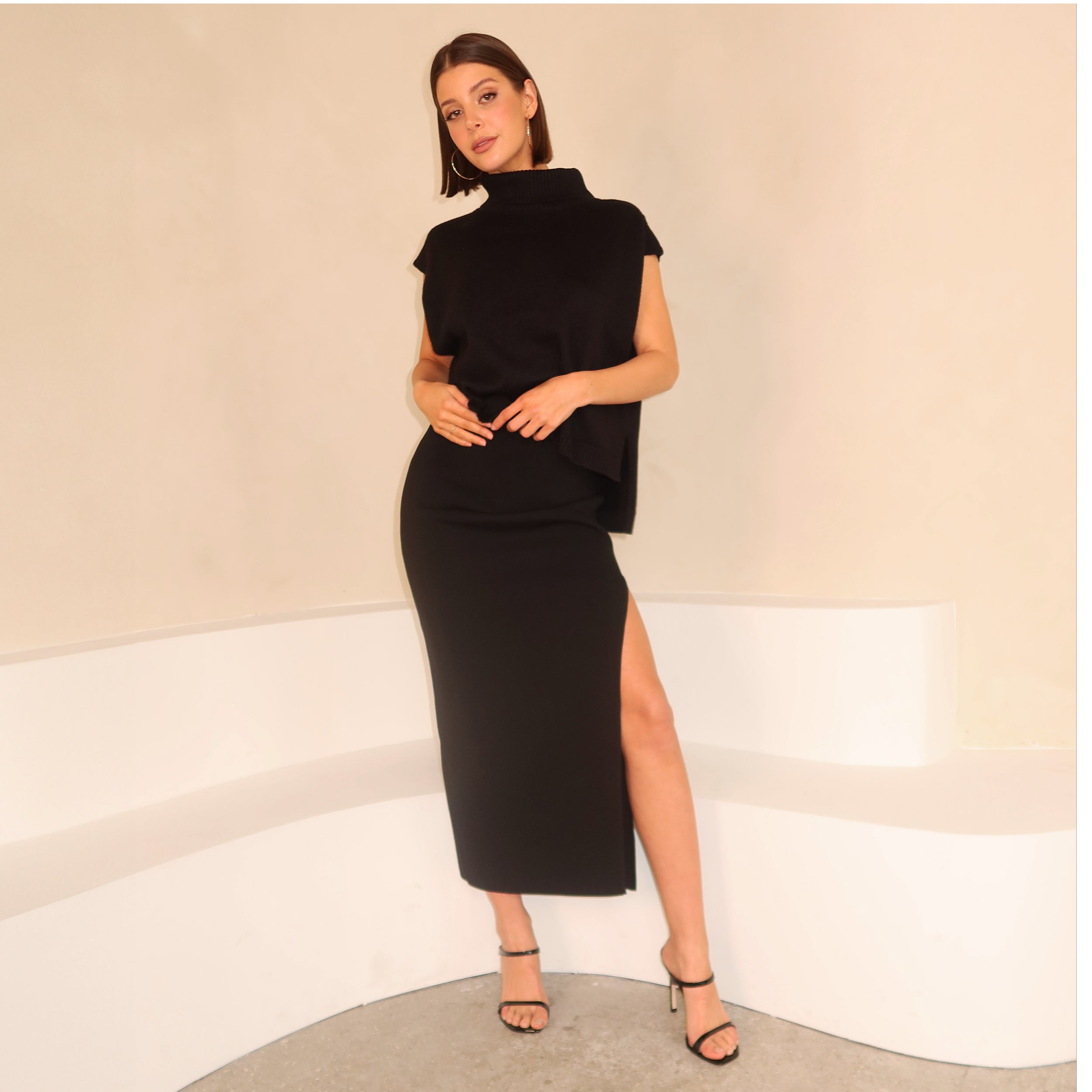 Full body view of woman wearing black sleeveless sweater and midi skirt with side slit