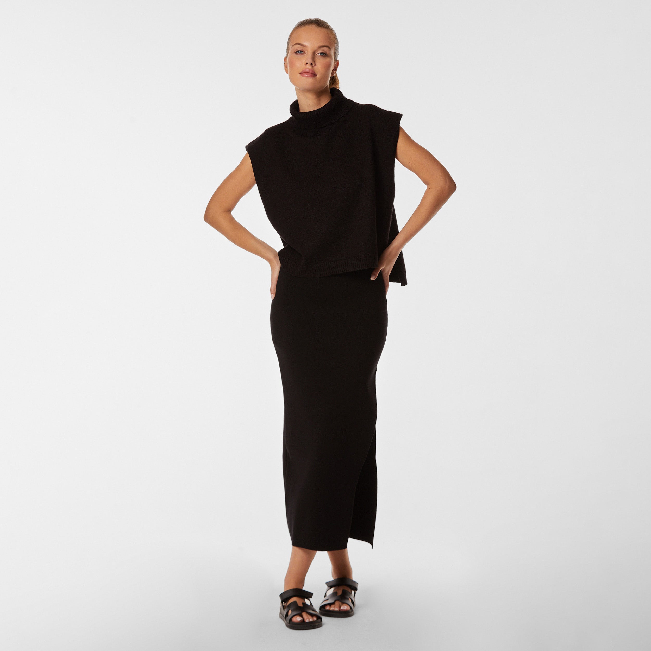 Full body front view of woman wearing sleeveless black sweater and black midi skirt