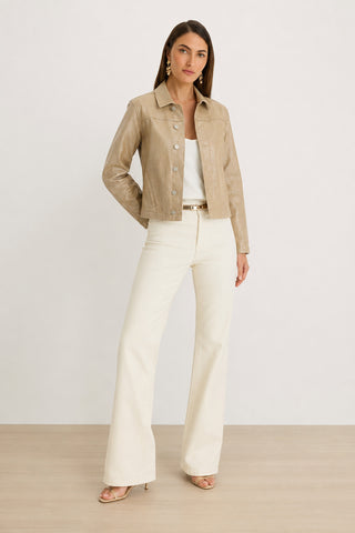 A woman stands on a wood floor wearing the Joelle Jean Jacket - Champagne over a white top, cream wide-leg pants, beige heels, and gold earrings, posing against a plain light background.