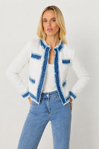 Wearing the Julia Tweed Jacket in Denim/White over a white top and light blue jeans, this woman stands confidently with her hands on her hips against a simple light background—a stylish summer layering look.
