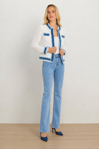 A woman stands on a wooden floor against a plain light background, wearing the Julia Tweed Jacket - Denim/White over a white top with light blue jeans and blue high heels—a chic example of summer layering.