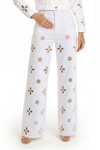 A woman wears the Kaia Pearl High Rise Jean - White, featuring wide legs and floral cutouts with pearl embellishments, paired with a matching floral cutout top for a fresh, summery look.