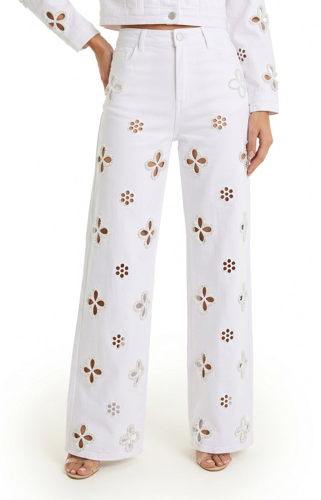 A person wears the Kaia Pearl High Rise Jean in white—high-waisted, wide-leg stretch denim with floral cutouts—paired with a matching long-sleeve jacket and open-toe sandals. Only the lower half of their body is visible.