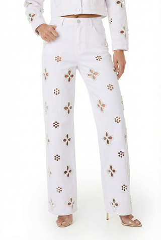 A woman wearing Kaia Pearl High Rise Jean in white with floral cutouts, paired with a matching jacket and nude high-heeled sandals.