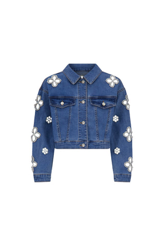 The Kaia Pearl Jean Jacket in medium blue is a cropped denim jacket with silver buttons, white and silver floral embellishments on the shoulders, chest, and sleeves. It features two front pockets and long sleeves.