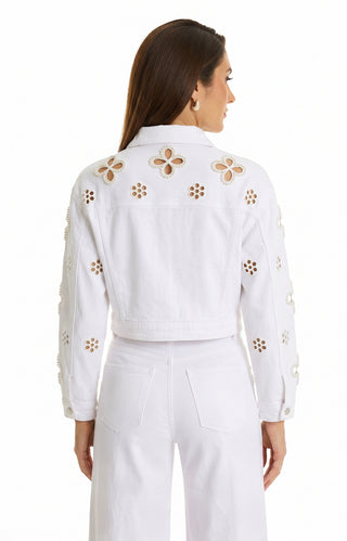 A woman with brown hair wears the Kaia Pearl Jean Jacket - White, featuring floral beadwork and cutout designs on the back and sleeves, styled with high-waisted white pants as she faces away.