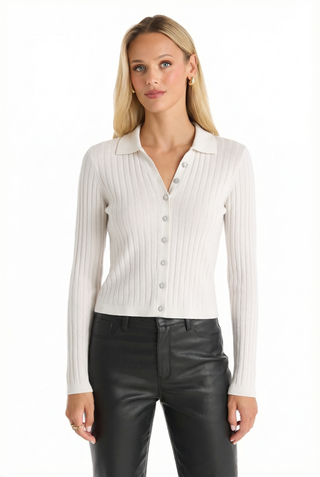 A woman with long blonde hair wears the Karolina Polo Shirt in white and black leather pants, standing against a plain white background.