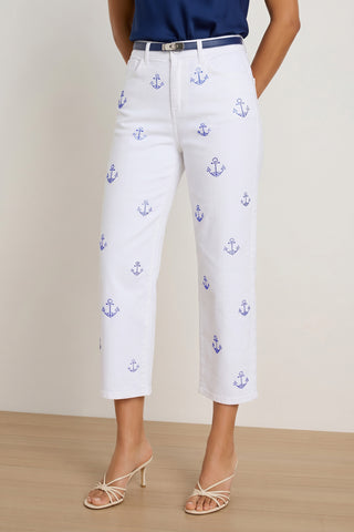 A person wears the Kelsey Cropped Jean - Crystal Anchors in white, paired with a navy belt, dark blue top, and strappy heeled sandals, standing on a wooden floor against a light background.