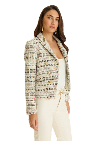A woman with long brown hair wears the Gabrielle Double Breasted Tweed Blazer - Ecru Multi, featuring gold buttons, over a white top and cream pants, standing against a white background.