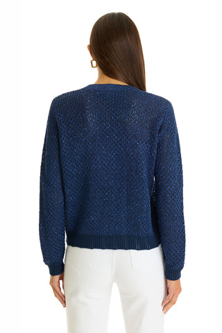 A woman with long brown hair wears the Shannon Sequin Cardigan Top in navy, featuring gold dome buttons, and white pants, shown from the back against a plain white background.