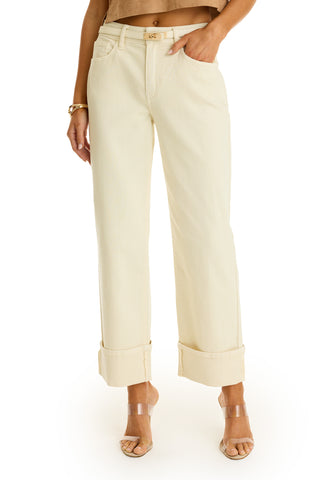 A person stands against a white background wearing the Ren Cropped Cuff Jean in Ivory, styled with a tan top, clear heeled sandals, and a gold bracelet.
