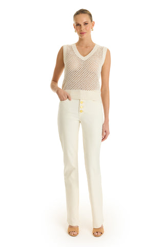 A woman stands against a white background wearing the Addison Sequin Crochet Top in Pearl, a resort-ready, sleeveless knitted cream top, paired with high-waisted cream pants with large buttons and tan open-toe heels.