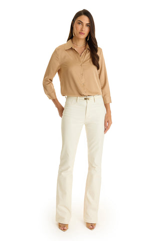 A woman with long dark hair and a neutral expression stands facing forward in the Sara Silk Blouse - Mocha, which features a high-low hem and long sleeves, paired with white high-waisted flared pants against a plain white background.