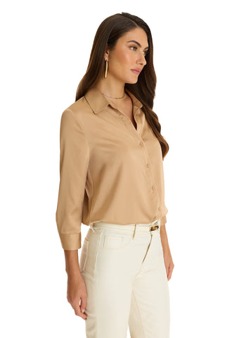 A woman with long brown hair models the Sara Silk Blouse in Mocha, featuring a lightweight design and three-quarter sleeves, paired with white pants. She stands angled to the side against a white backdrop.