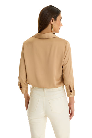 A woman with long brown hair, wearing the Sara Silk Blouse in Mocha and white pants, stands facing away from the camera against a white background.