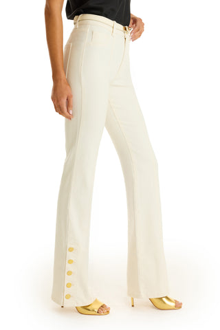 Only the lower body is visible, featuring the Veronica Button Jean - Ivory: high-waisted, cream flared pants with gold buttons on the outer hem, paired with a black top and gold open-toe heels for a leg-lengthening look.