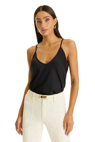 A woman in the Yara Silk Camisole - Black and high-waisted white pants with a belt stands against a white background, facing forward with her hand by her side.