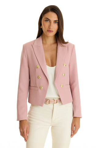 A woman wears the Gabrielle Double Breasted Blazer - Blush, featuring a tailored waist and gold buttons, over a white top and cream pants against a plain white background.