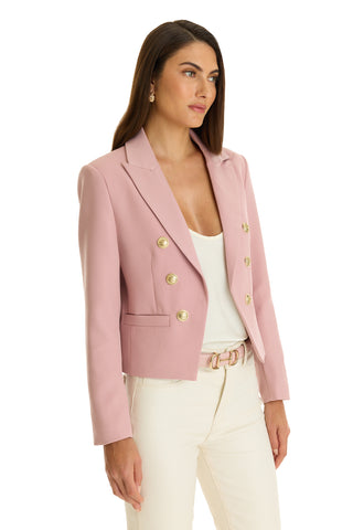 A woman wears the Gabrielle Double Breasted Blazer - Blush with a tailored waist and gold buttons, paired with a white top and cream pants, standing against a plain white background.