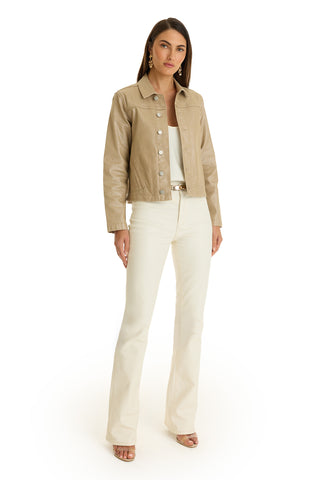 A woman faces forward in the Joelle Jean Jacket - Champagne over a white top and high-waisted pants, paired with open-toe heels. She has straight brown hair, minimal makeup, and gold earrings, standing against a white background.