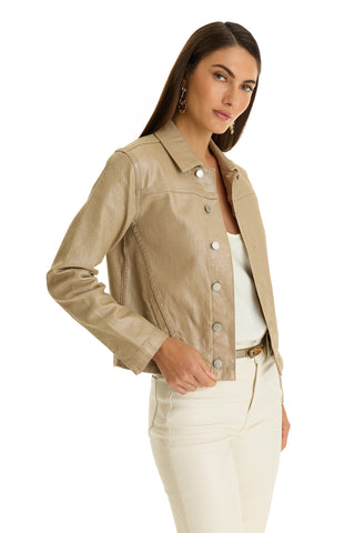 A woman with long brown hair models the Joelle Jean Jacket in Champagne—a slim-fit, beige faux leather button-up—over a white top and cream pants, standing against a white background and holding the jacket while facing the camera.