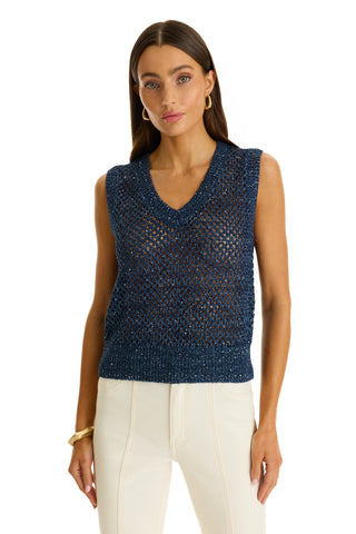 A woman stands against a white background wearing the resort-ready Addison Sequin Crochet Top in navy, styled sleeveless with a V-neck, paired with white high-waisted pants, gold hoop earrings, and a gold bangle.